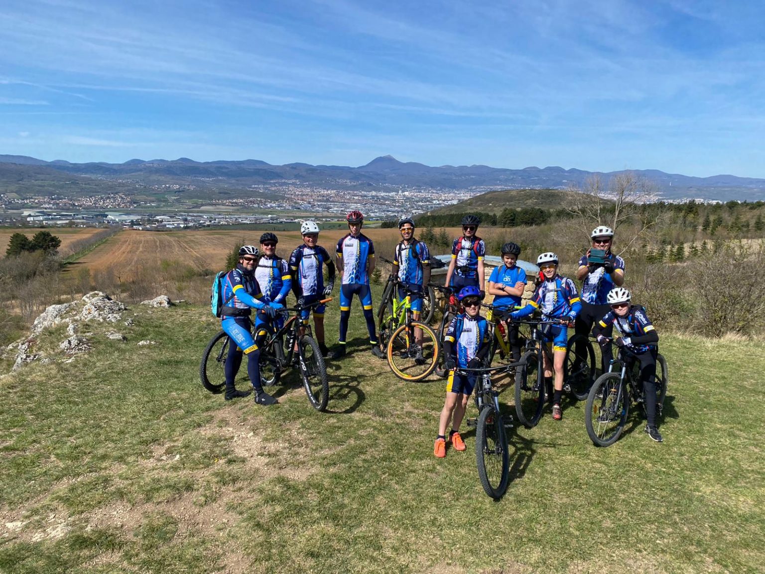 Une douzaine de vététistes du club en maillot, avec la plaine de la Limagne en arrière-plan